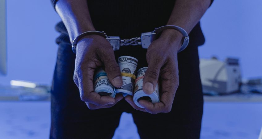 Close-up of handcuffed hands holding rolled cash, suggesting crime or arrest.