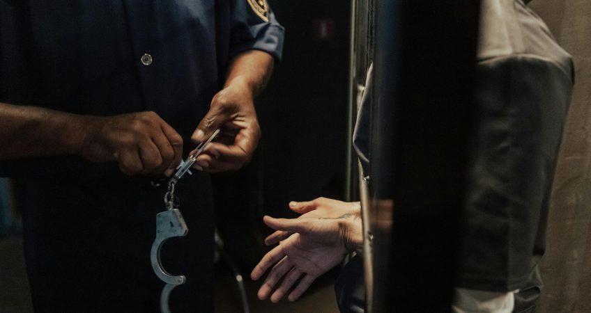 A police officer handcuffing a suspect through bars indoors, signifying arrest and law enforcement.